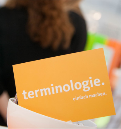 Eine orange Postkarte mit dem Spruch "Terminologie. Einfach machen."