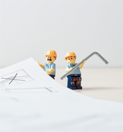 Technische Übersetzung; zwei erschrockene Lego-Bauarbeiter halten eine Anleitung und einen Inbusschlüssel