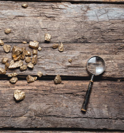 Term Mining; Gold Nuggets und eine Lupe auf einem alten Holztisch