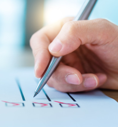 Übersetzungsgerechtes Schreiben; Hand mit Stift, die Kästchen auf einem Blatt abhakt